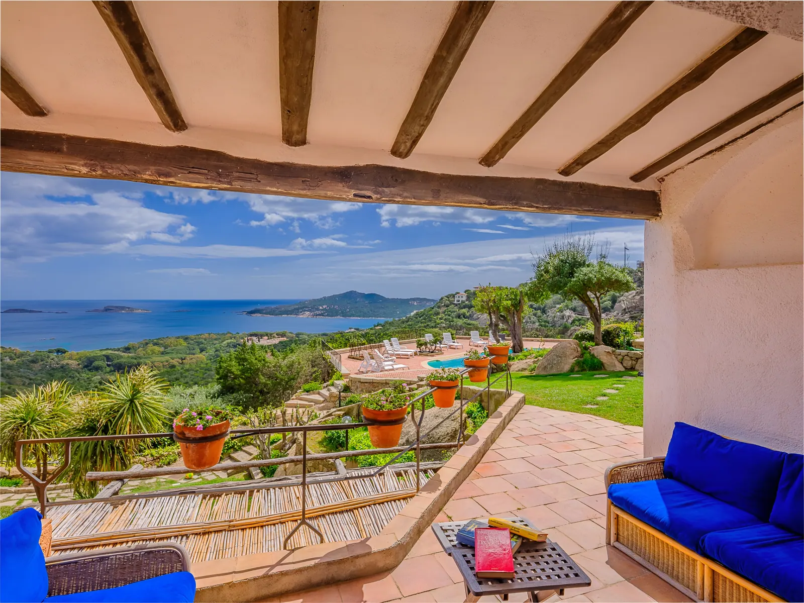 La veranda di Villa Carmen 1 a Porto Cervo: divani blu, travi di legno e il mare in fondo